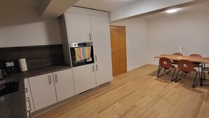 Moderni keittiö, jossa on valkoiset kaapit, sisäänrakennettu uuni sekä ruokailutila, jossa on puinen pöytä ja neljä tuolia.