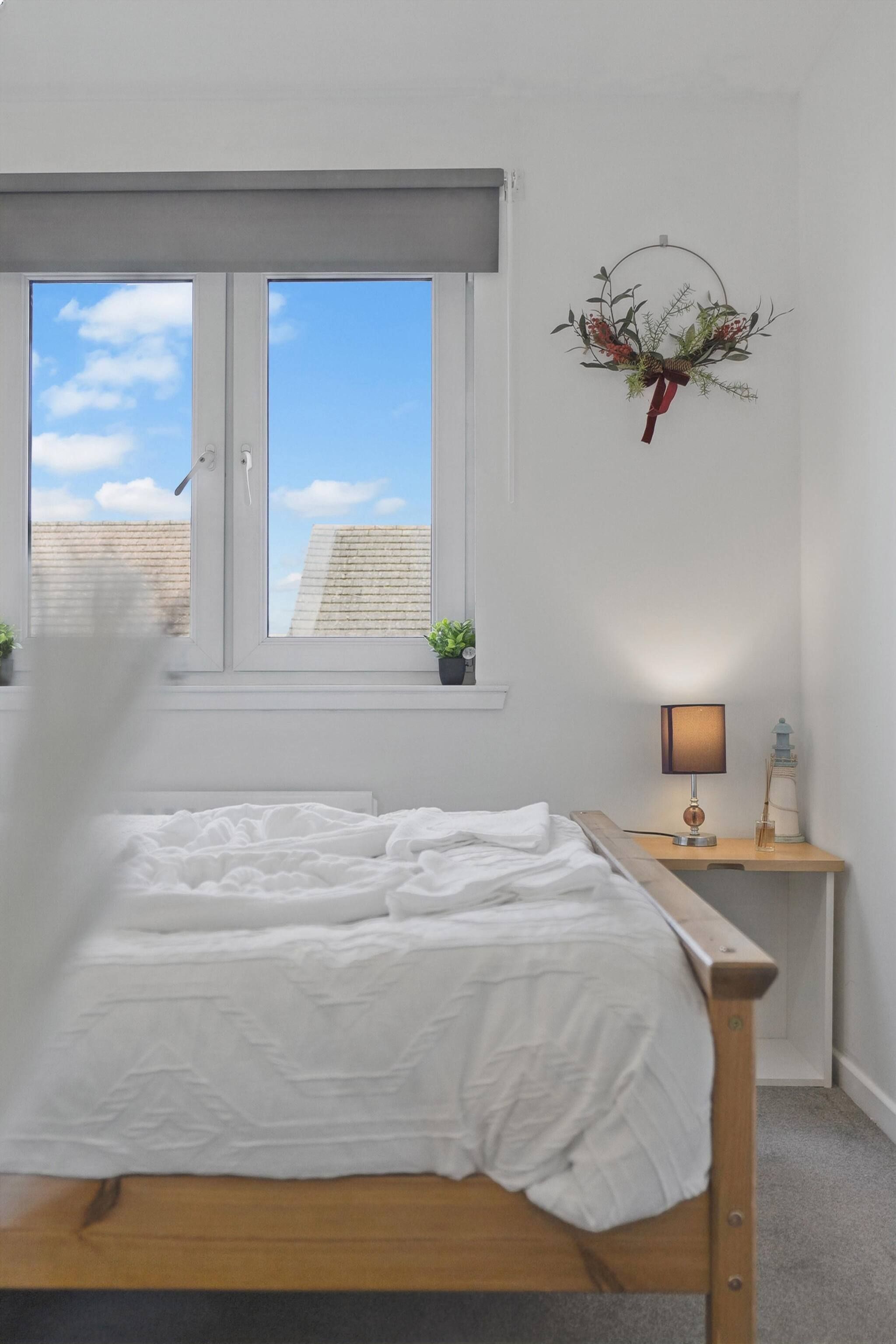 Une chambre à coucher comprenant un lit, une fenêtre, une table de chevet avec une lampe et un élément décoratif fixé au mur.
