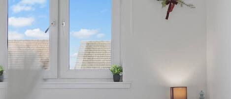 Une chambre à coucher comprenant un lit, une fenêtre, une table de chevet avec une lampe et un élément décoratif fixé au mur.