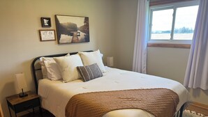 Een keurig opgemaakt bed met kussens, een bedlamp en een lijst met een afbeelding aan de muur.