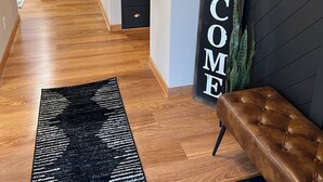Een moderne woonkamer met een bank, een zwart tapijt, een zitbankje en een 'WELCOME' bord aan de muur.