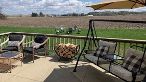 Een terras met rieten stoelen, een schommel en een tafel, met uitzicht op een veld.