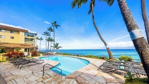 Uma área de piscina com espreguiçadeiras, um pátio de pedra e vista para o oceano.