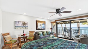 Quarto com uma cama grande, ventoinha no teto, varanda com vista para o oceano e área de jantar com mesa e cadeiras.