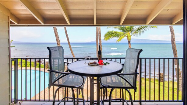 Área externa coberta com mesa e cadeiras, com vista para uma piscina e oceano.