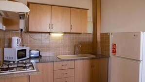 Een kleine keuken met houten kastjes, een magnetron, een gasfornuis, een spoelbak en een koelkast.