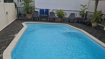 Una piscina rectangular con borde de azulejos, rodeada por una zona pavimentada con sillas y plantas en macetas.