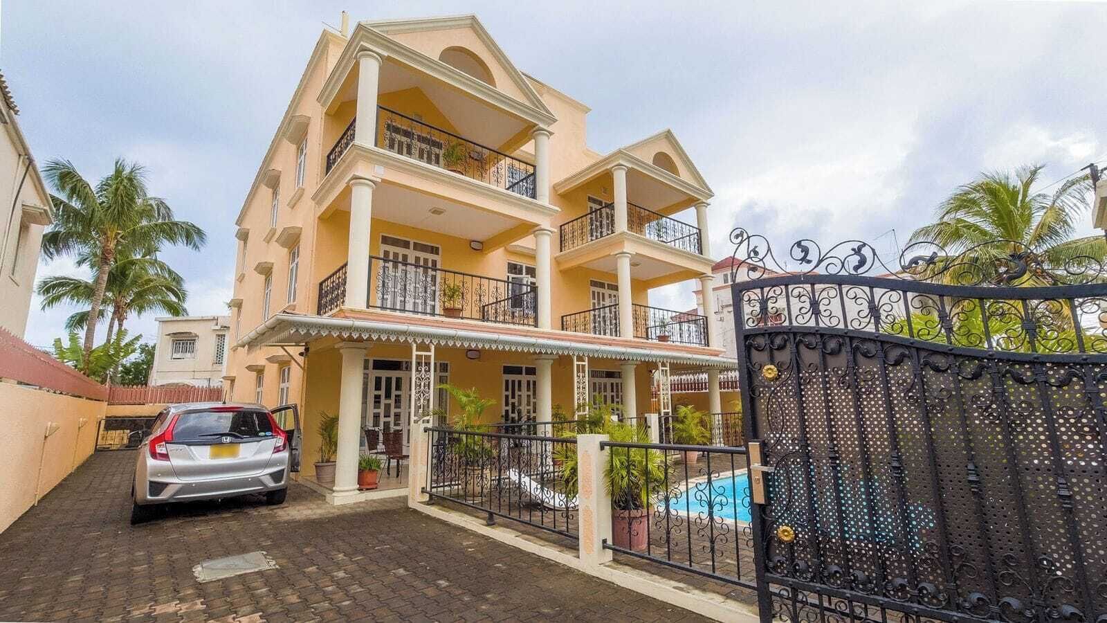 Un edificio residencial de varios pisos con balcones, entrada protegida por un portón y una piscina.