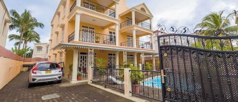 A multi-story residential building with balconies, a gated entrance, and a swimming pool.