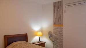 Een slaapkamer met een bed, een bedlamp, een ventilator aan de muur en een metselwerk wand.