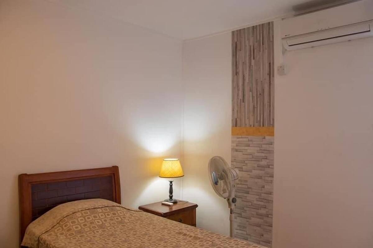 Une chambre à coucher avec un lit, une lampe de chevet, un ventilateur fixé au mur et un mur décoré d’un motif en briques.