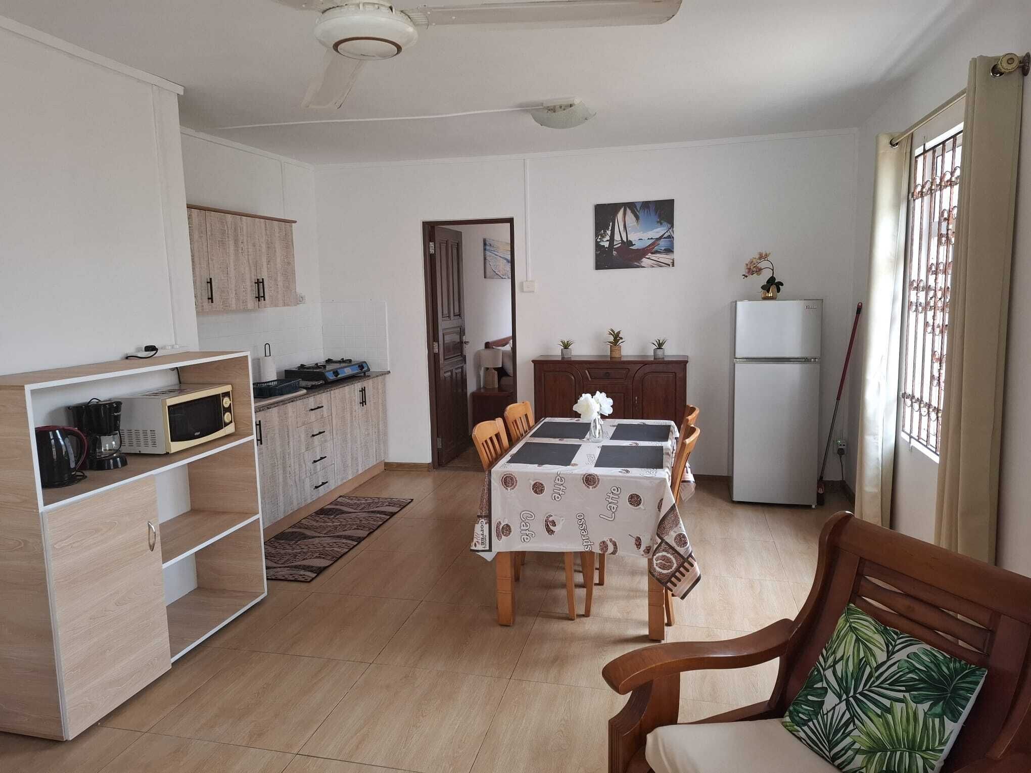 A compact kitchen with a dining area, wooden cabinets, a refrigerator, and a window with curtains.