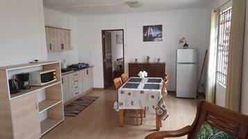 A compact kitchen with a dining area, wooden cabinets, a refrigerator, and a window with curtains.