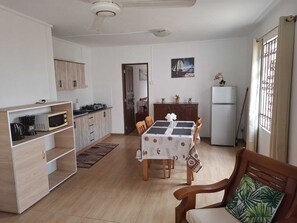 A compact kitchen with a dining area, wooden cabinets, a refrigerator, and a window with curtains. - Résidence le Palmier (Mont Choisy)