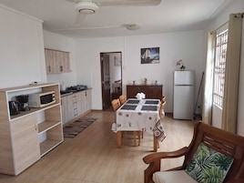 A compact kitchen with a dining area, wooden cabinets, a refrigerator, and a window with curtains.