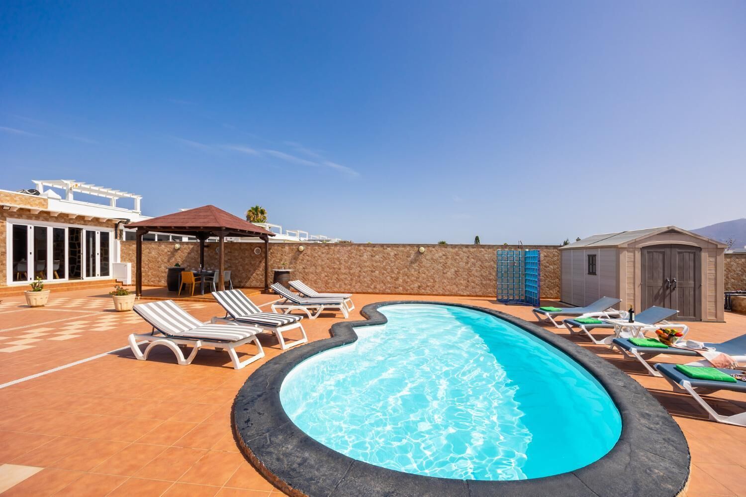 Una piscina en la azotea con sillones de descanso, una pérgola y un edificio pequeño.