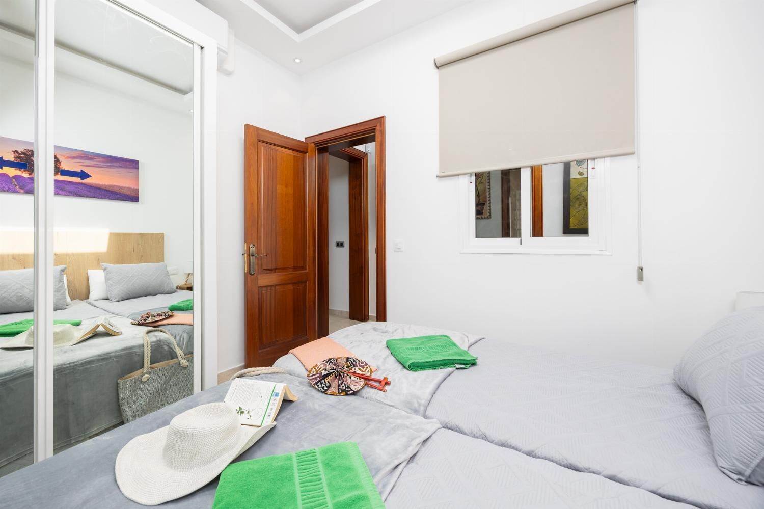 A bedroom with a bed, a wardrobe, a window with a blind, and a painting on the wall.