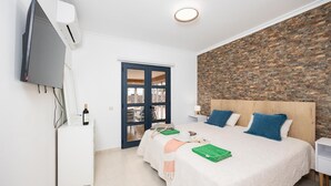 Hotellihuone, jossa on sänky, televisio, työpöytä, vaatekaappi ja kiviseinä.