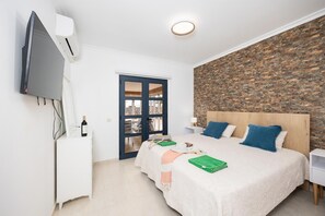 A hotel room with a bed, a TV, a desk, a wardrobe, and a stone wall. - Villa Marisol with air con and private heated pool (Playa Blanca)