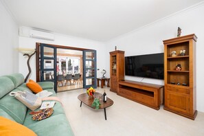 A living room with a sofa, coffee table, TV, wooden cabinet, and a dining area visible through an open door. - Villa Marisol with air con and private heated pool (Playa Blanca)