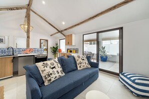 A modern living room with a blue sofa, a striped pillow, and a kitchen in the background. - Stylish 3BR penthouse home covering townhouse floor, near Portimão promenade, 15 mins to Praia da Rocha. Private unit in historic building with large private Terrace, AC in all bedrooms, fast Wi-Fi, and modern comforts. (Portimao)