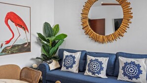 Ein Zimmer mit einem blauen Sofa, dekorativen Kissen, einem gerahmten Gemälde, einem großen Spiegel und einer Topfpflanze.