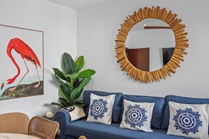 Ein Zimmer mit einem blauen Sofa, dekorativen Kissen, einem gerahmten Gemälde, einem großen Spiegel und einer Topfpflanze.