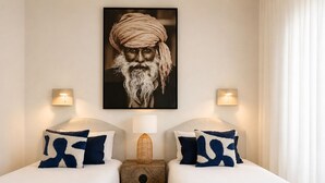 Ein Hotelzimmer mit zwei Betten, einem Holfnachtkästchen, einer Wandlampe und einem gerahmten Bild über den Betten.