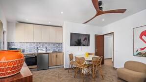 Eine moderne Küche mit Holzausbau, ein Essbereich mit Korbstühlen, einem Deckenventilator und einem großen Gemälde.