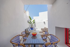 A narrow outdoor patio with a table and chairs, a potted plant, and a view of a white building. - Beautifully refurbished ground Townhouse, one of two independent homes in Alvor Old Town. Steps from the waterfront, restaurants and beach, with 2 bedrooms, AC throughout, and access to sunny terraces, Jacuzzi Bath and sea views. (Portimao)