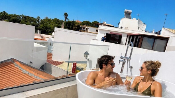 Een terras op het dak met een jacuzzi, uitzicht over de buurt en een heldere lucht.