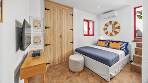 Een slaapkamer met een bed, een ronde spiegel, een houten garderobe, een klein krukje en een aan de muur bevestigde televisie.