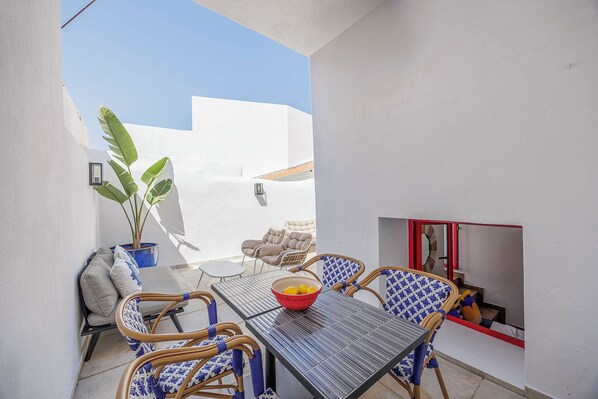 A patio with a table and chairs, a potted plant, and a red-framed window. - Beautifully refurbished ground Townhouse, one of two independent homes in Alvor Old Town. Steps from the waterfront, restaurants and beach, with 2 bedrooms, AC throughout, and access to sunny terraces, Jacuzzi Bath and sea views. (Portimao)