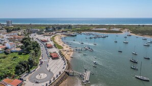 Vista aerea di una cittadina costiera con un porto turistico, edifici e una strada.