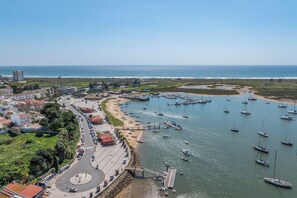 Luchtbeeld van een kustplaatsje met een jachthaven, gebouwen en een weg.