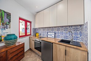 Een kleine keuken met houten kastjes, een zwarte spoelbak en een betegelde achterwand.