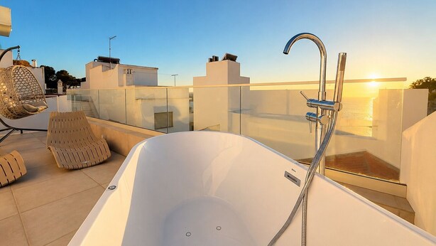 Una terrazza panoramica con una vasca da bagno bianca, una sedia a dondolo e un parapetto in vetro.