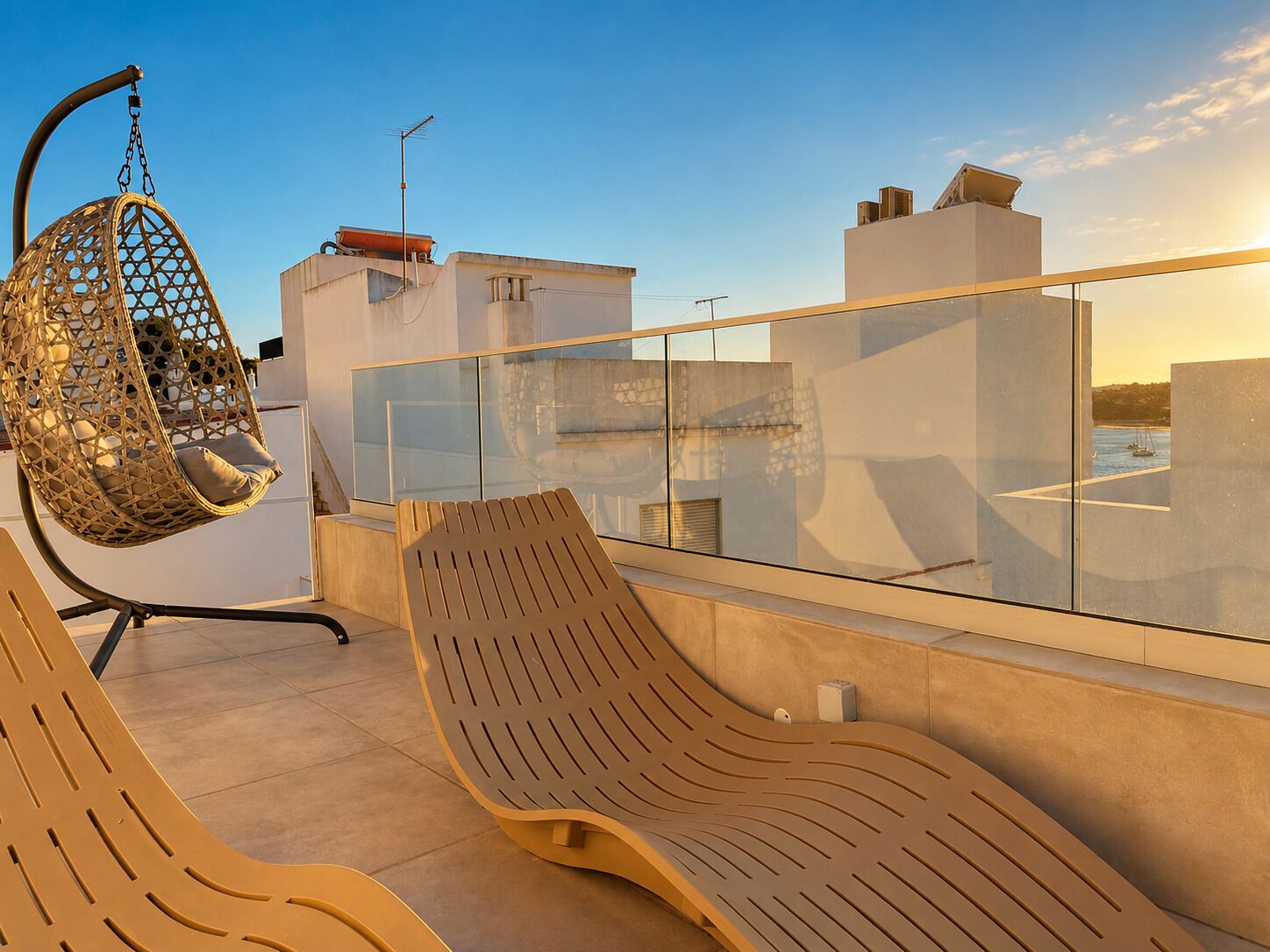 A rooftop terrace with a hanging chair, a lounge chair, and a glass balustrade.