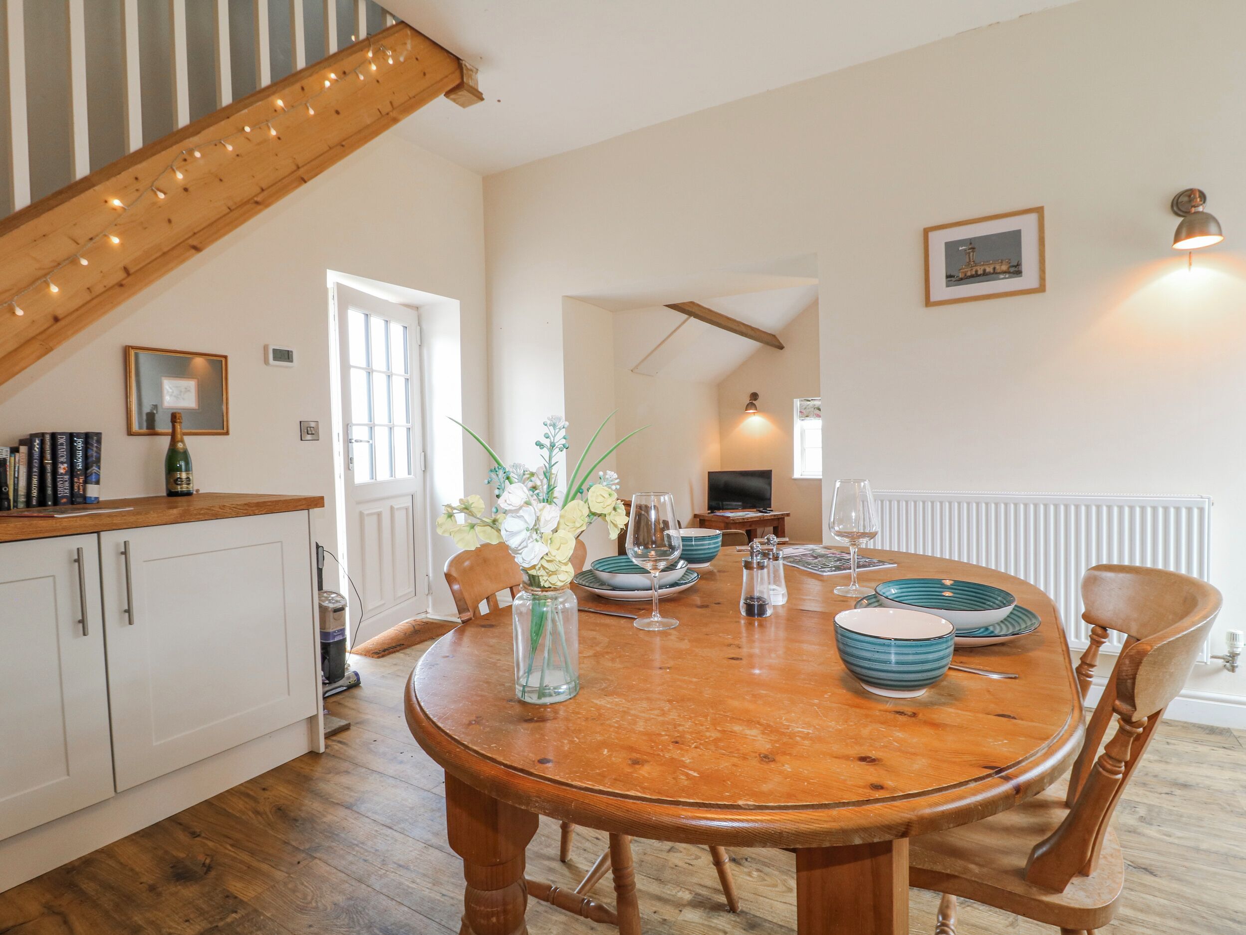 A dining area with a wooden table, chairs, a vase with flowers, and a bottle of champagne.