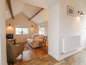A cozy living room with a sofa, a chair, a TV, and a fireplace. - The Granary Barn at America Lodge (Oakham)