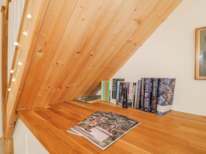 A wooden sloped ceiling with string lights, a wooden bench, and a row of books on the wall.