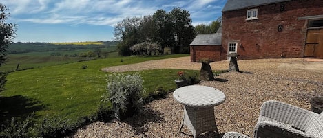 A rustic brick house with a gravel patio, outdoor seating, and a view of the countryside.