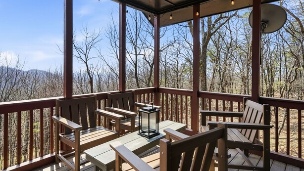 A covered outdoor deck with wooden furniture and a lantern, overlooking a forested area. - Mtn Resort Getaway - 4 Bed, 3 Bath - Lake with Kayaks , Golf, Pools, Pickleball (Jasper)