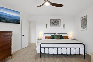 Une chambre à coucher comprenant un lit, des tables de chevet, une commode et un ventilateur de plafond.