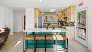 A modern kitchen with a central island, bar stools, wooden cabinets, and a view through the window. - Mtn Resort Getaway - 4 Bed, 3 Bath - Lake with Kayaks , Golf, Pools, Pickleball (Jasper)