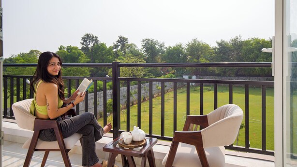 Een balkon met uitzicht op een groen gazon, een tafel met theepot en kopjes, en twee stoelen.