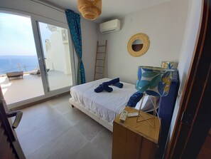 Une chambre à coucher avec un lit, une table de chevet avec une lampe, une fenêtre avec des rideaux, un appareil de climatisation et une vue sur l’extérieur.