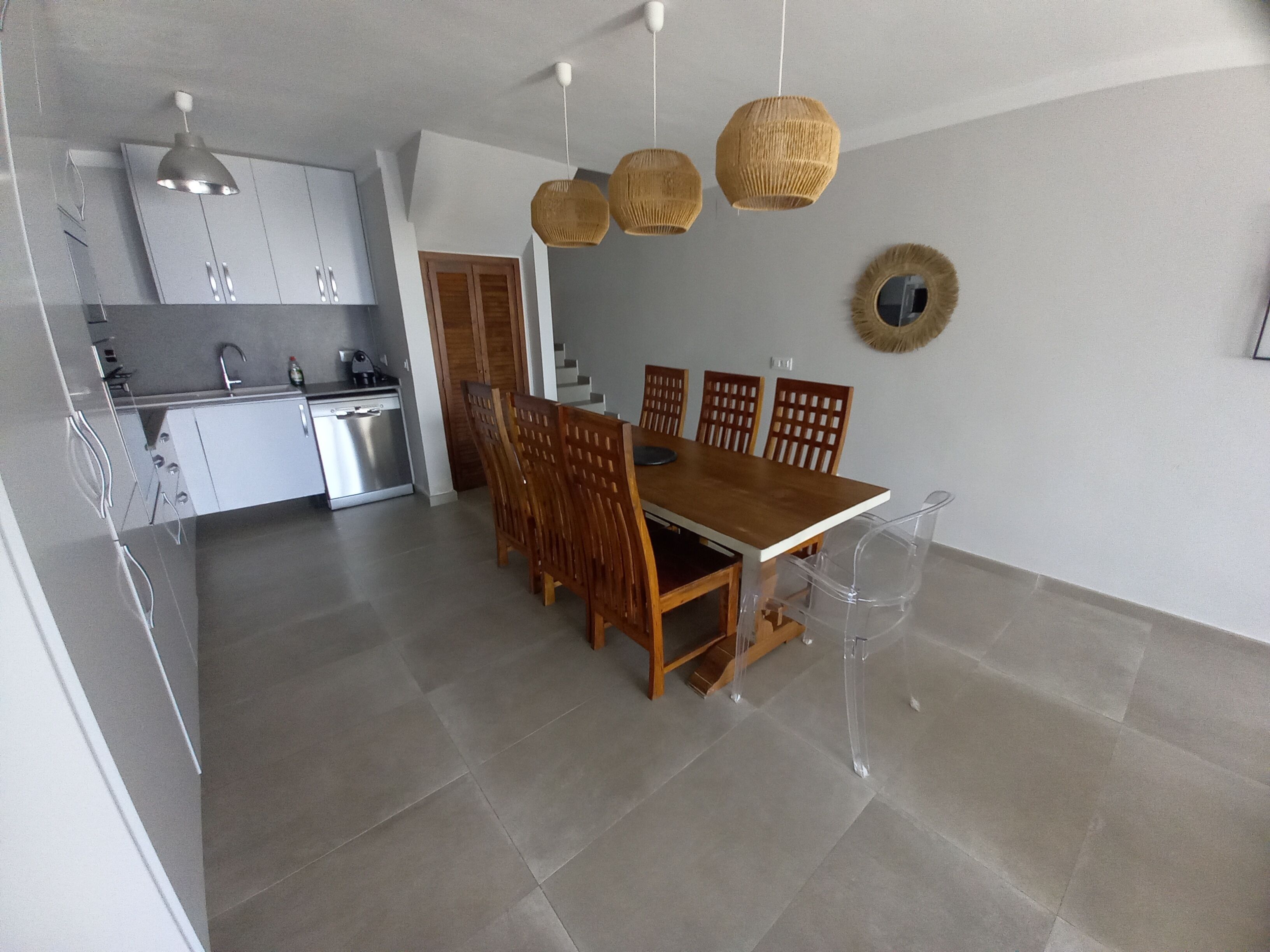 A modern kitchen with white cabinets, a dining area with wooden chairs and a table, and a staircase leading to an upper floor.