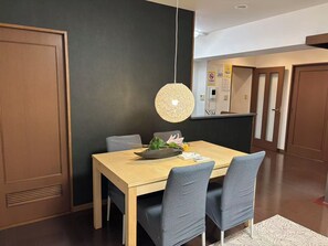 A dining area with a wooden table, blue chairs, a hanging light fixture, and a kitchen in the background. - 5 min walk from Nishi-Shinjuku 5-chome station, large family of 7, loop balcony (新宿区)