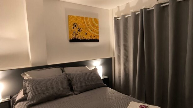 Ein ordentlich bezogenes Bett mit Kopfteil, Nachttischlampe und einem Wandbild.
